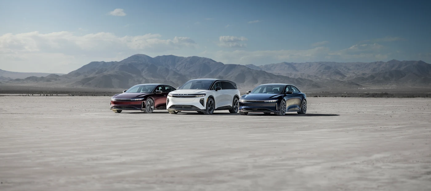Three stylish electric vehicles in red, white, and blue parked on a barren landscape with mountains in the background.
